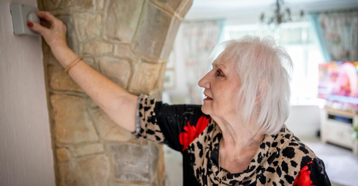 Elderly woman with gray hair adjusting temperature controller indoors