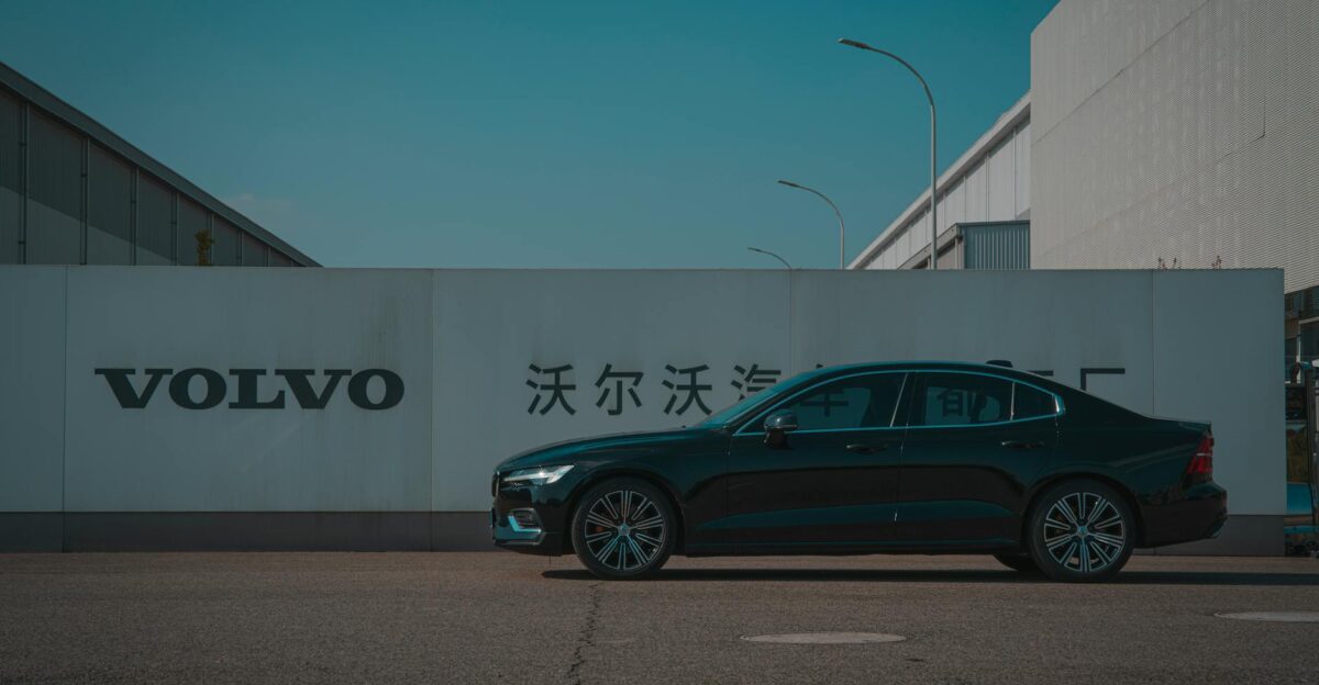 Sleek black Volvo sedan parked outside a manufacturing plant with Volvo signage