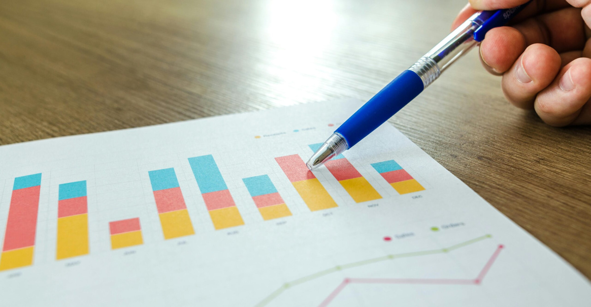 Detailed close-up of a hand pointing at colorful charts with a blue pen on wooden surface.