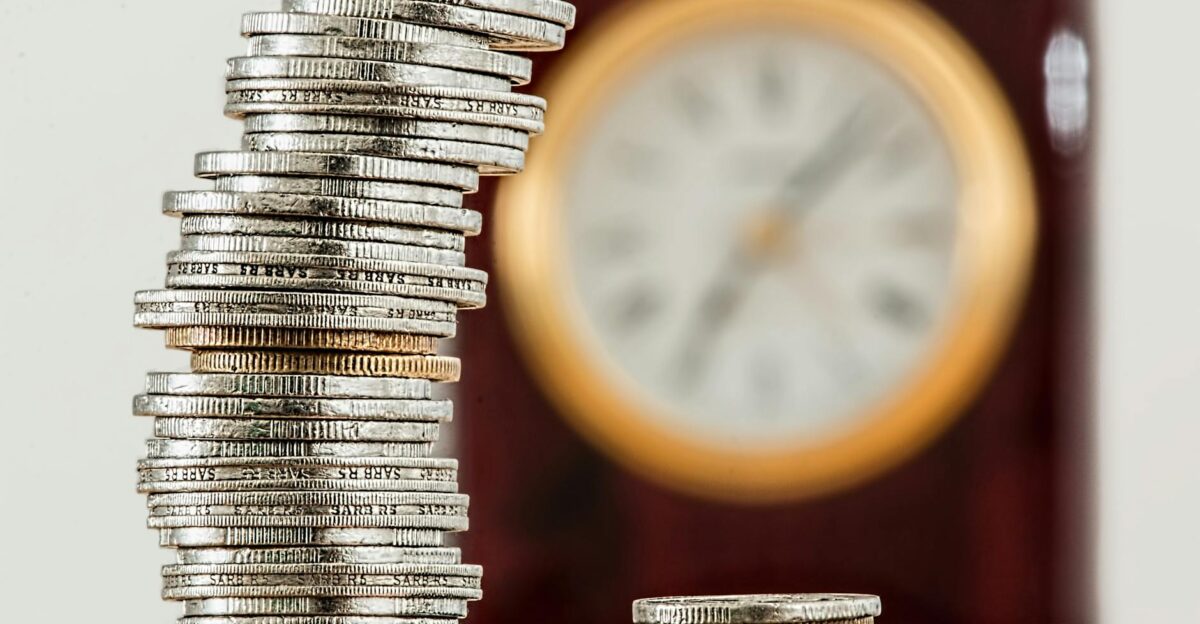A close-up image of stacked coins with a blurred clock symbolizing time and money relationship