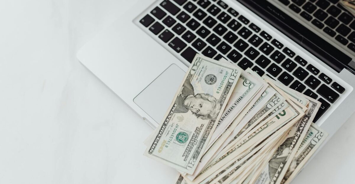 A stack of US dollar bills on a laptop keyboard representing online finance and budgeting