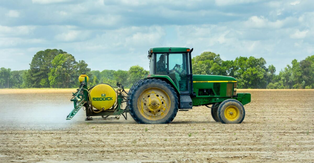 Green tractor with sprayer working in an open farm field under a cloudy sky