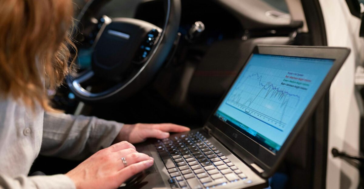 Female engineer using laptop to analyze vehicle data inside a car for testing purposes