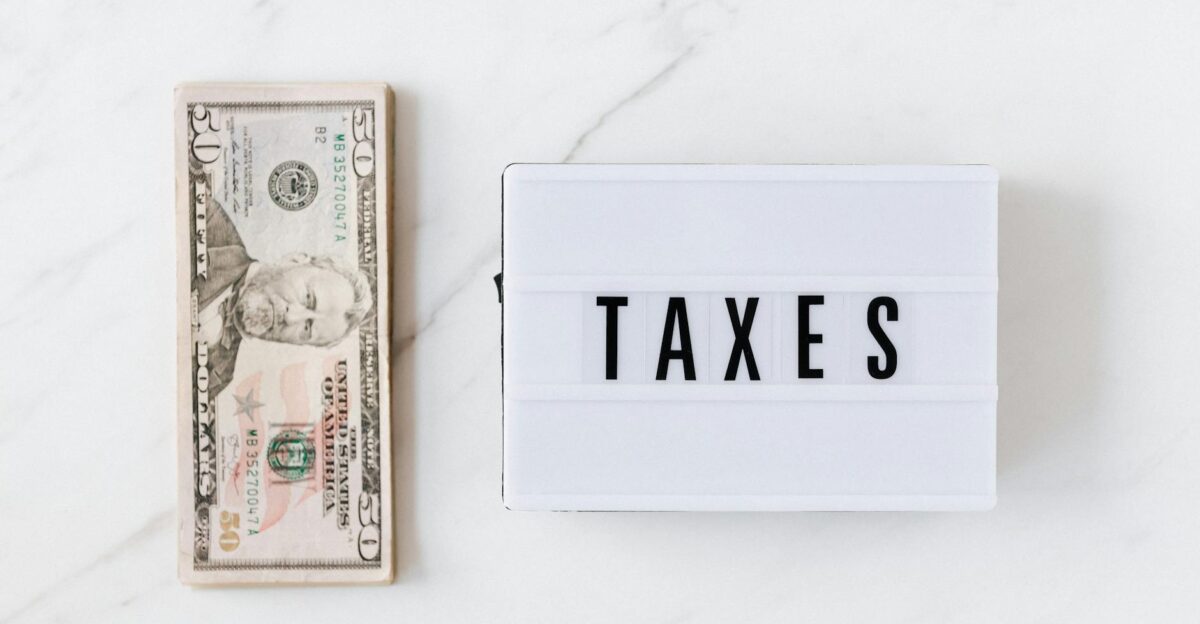 Overhead view of a fifty-dollar bill and a lightbox with TAXES on a marble surface