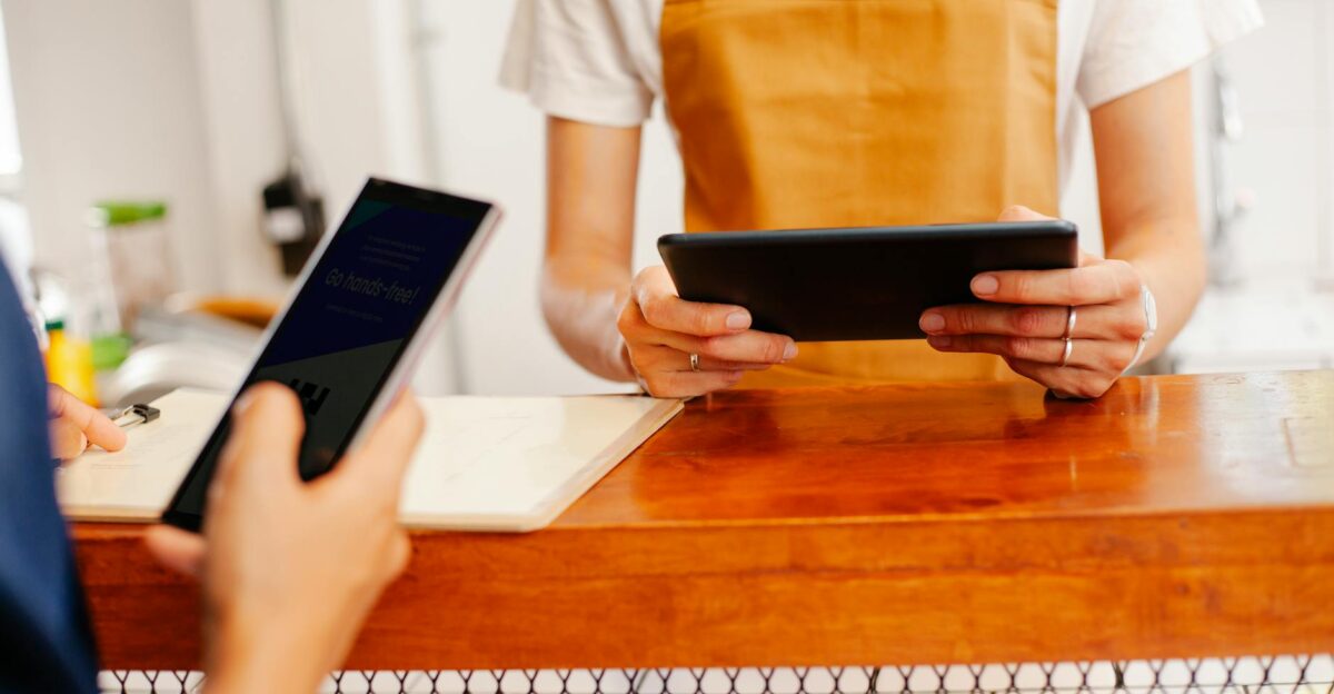 A barista in an apron uses a tablet in a small cafe Customer interaction at the counter