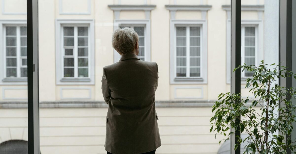 A professional woman gazes thoughtfully through an office window lost in contemplation