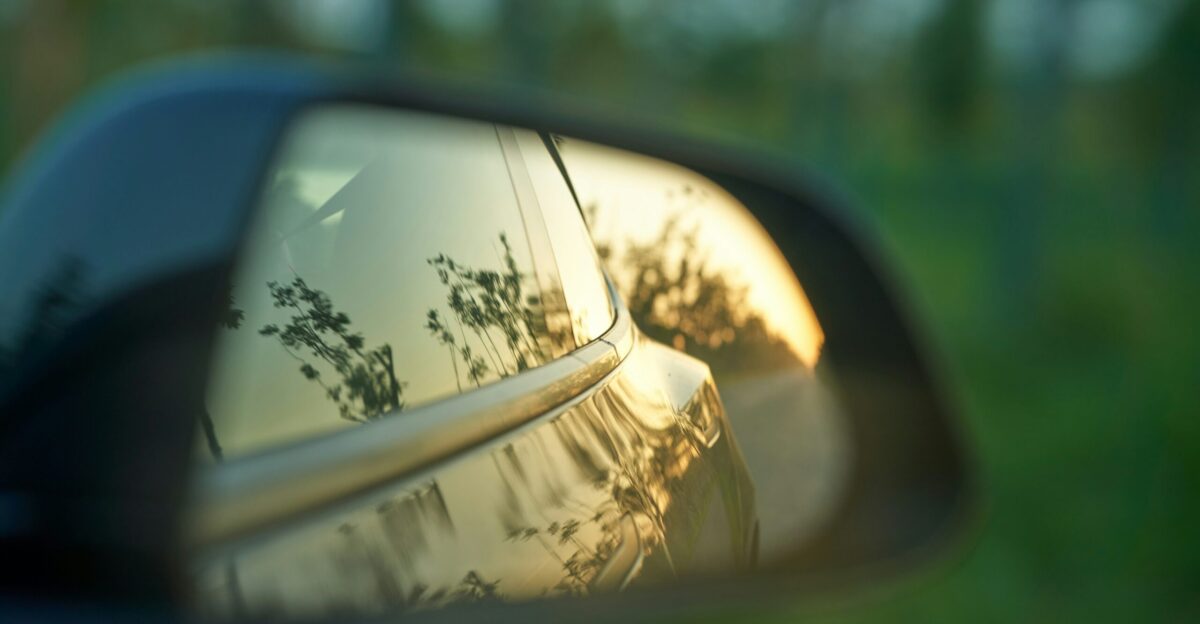 a car s side view mirror reflecting the trees in the rear view mirror