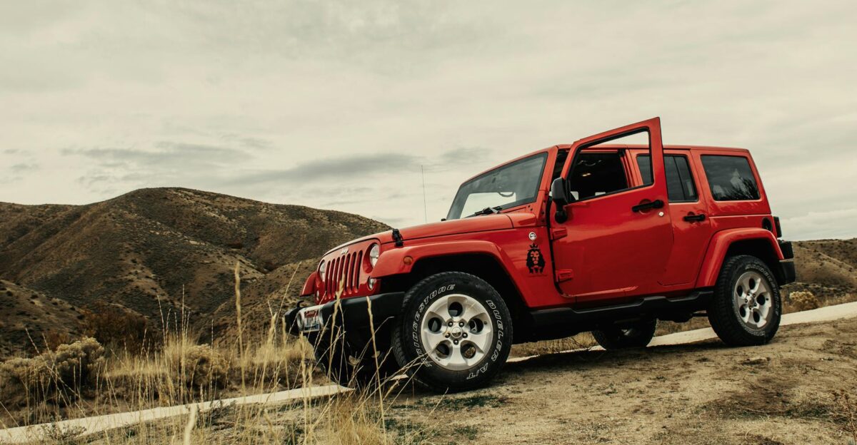 A vibrant red SUV parked on a dirt road with a mountain landscape backdrop under a cloudy sky