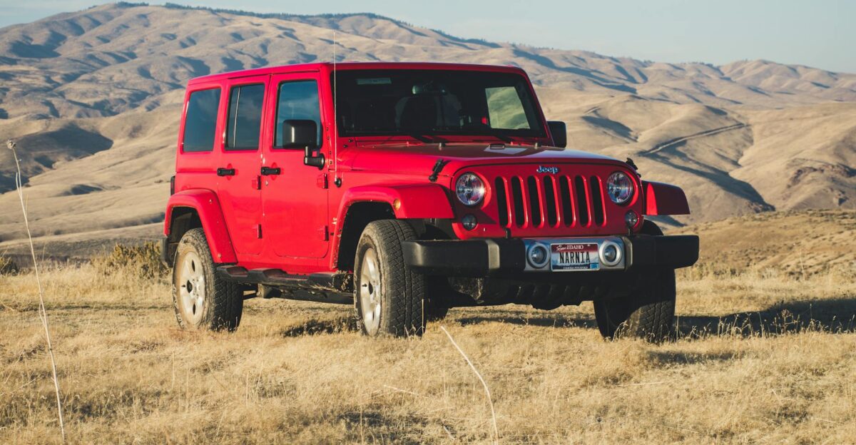 A striking red Jeep Wrangler parked in a vast desert-like landscape under a clear sky