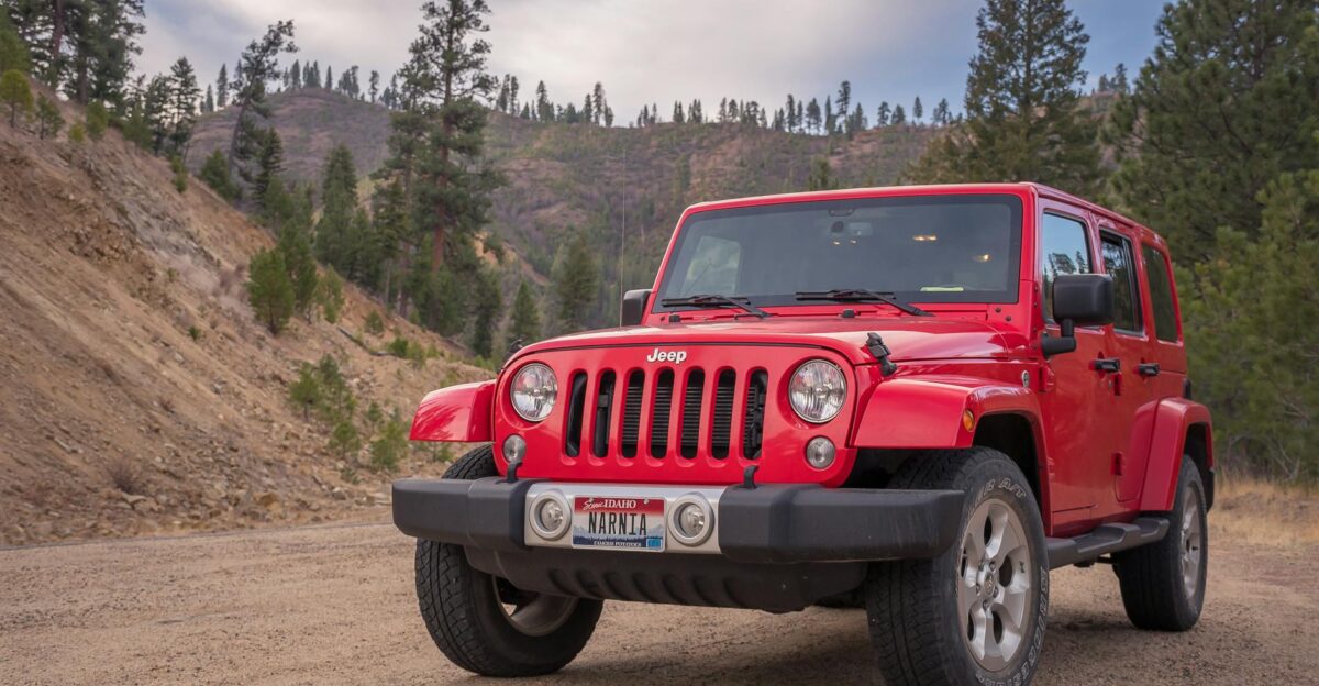 Red Jeep parked on dirt road with mountainous forest backdrop ideal for travel and adventure themes
