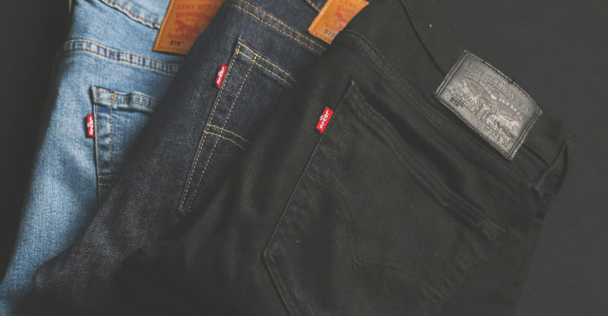 A stack of blue, dark, and black denim jeans folded on a dark surface.