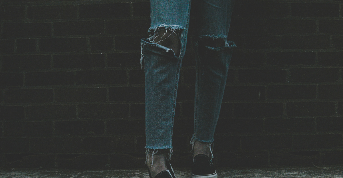 person wearing distressed blue denim jeans and pair of black-and-white sneakers