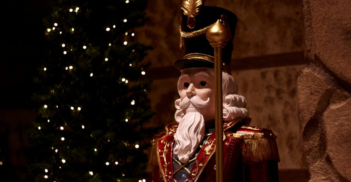 A festive nutcracker stands by a christmas tree